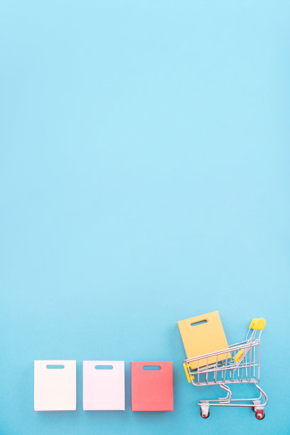抽象的设计元素，年度销售的概念，购物季-迷你黄色购物车与纸袋孤立在柔和的蓝色背景。图片下载