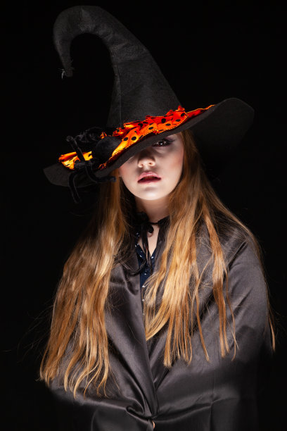 万圣节。女巫的帽子上有一只蜘蛛在黑色的背景。美丽的年轻惊讶的女人戴着女巫的帽子和服装。宽万圣节派对艺术设计。复制粘贴。女巫工艺概念。蜘蛛在帽子图片下载