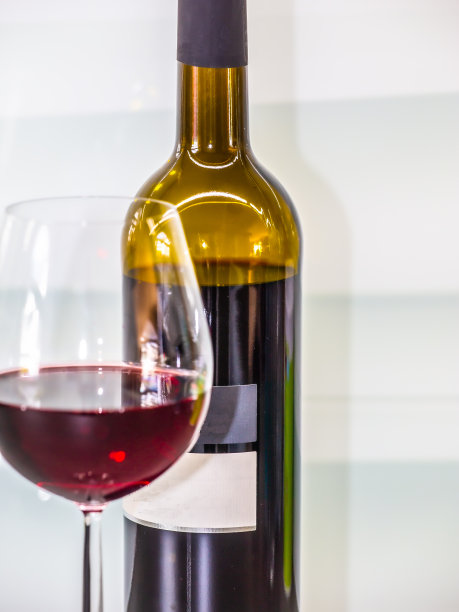 前面是一个模糊的盛满红酒的玻璃杯，后面是一瓶葡萄牙红酒图片下载