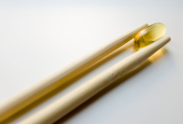 用筷子夹鱼油胶囊。鱼油胶囊。白色背景上的欧米茄3鱼油胶囊。高分辨率的产品。食物补充。-6， -9，维生素A, D, D3, E图片下载