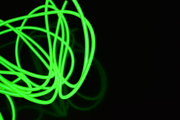 不同形状和结构的有毒绿色发光电致发光线。一种由石灰电致发光纤维、el线和特殊的圆圈组成的网，位于黑色光滑的表面上。图片下载