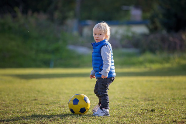 蹒跚学步的小男孩，在公园的操场上踢足球图片下载