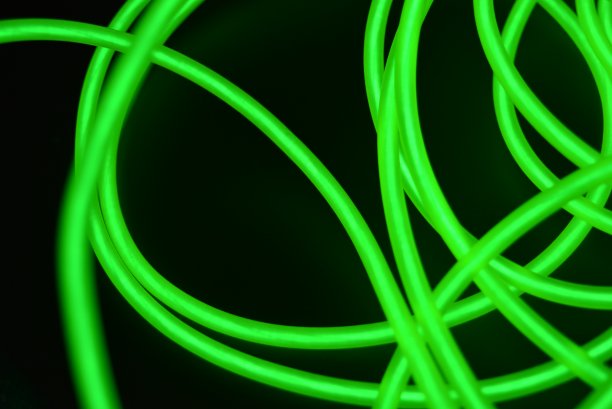 不同形状和结构的有毒绿色发光电致发光线。一种由石灰电致发光纤维、el线和特殊的圆圈组成的网，位于黑色光滑的表面上。图片下载