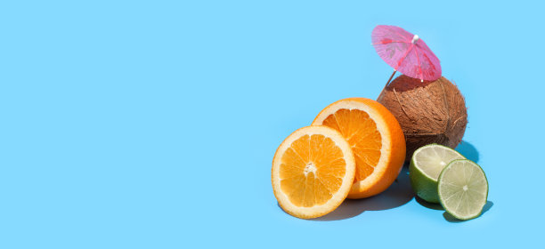新鲜多汁的橙子，椰子和青柠与鸡尾酒伞孤立在蓝色的背景。健康饮食和节食的概念。旅游和假日概念。副本的空间。为你的文本留出空间图片下载
