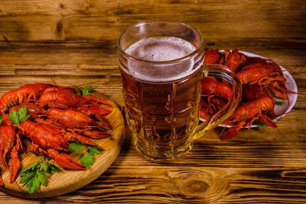 木桌上放着一杯啤酒和煮小龙虾图片下载