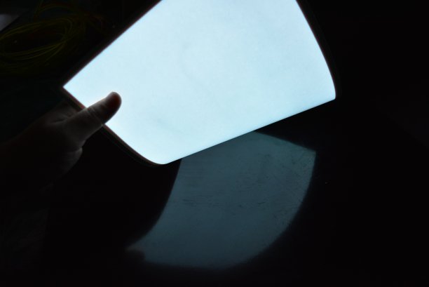 非常明亮和发光的A4电致发光纸与涂层位于不同的平面在一个原始光滑的表面与女性的手。优良的彩色基材，发光均匀。图片下载