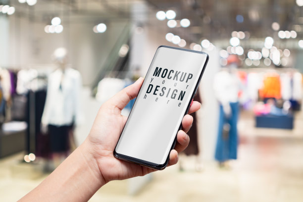 模拟手机形象的女人手持智能手机与空白白屏幕为您的广告在模糊抽象的背景女装时装店。图片下载