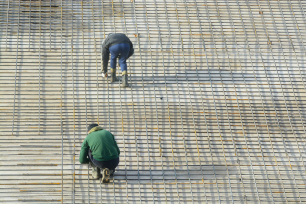 工人们在建筑物的地基上捆扎钢筋，形成一个网格。图片下载