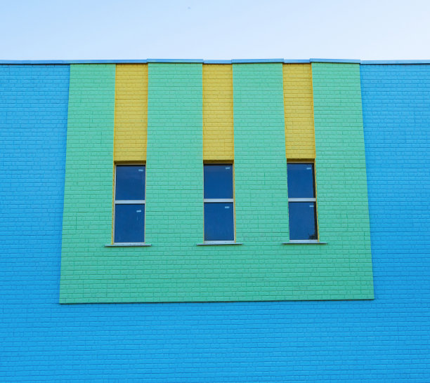 蓝色的砖墙上有三扇绿色和黄色的狭长垂直窗户图片下载