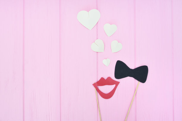 男人和女人坠入爱河的概念。女性的嘴唇和领结与心在粉红色的木制背景与地方的文字。婚礼、贺卡、情人节的创意图片下载