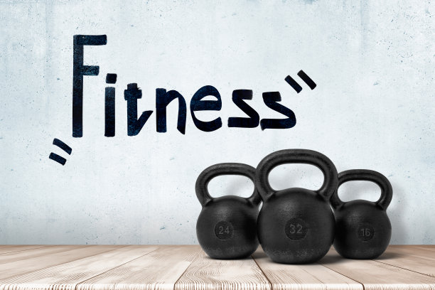 3d渲染的三个黑色壶铃在白色木地板上与“健身”标志上方的白色墙壁背景图片下载