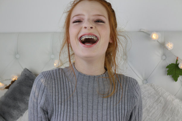 照片中，14 / 15岁的红发少女，皮肤苍白，脸上有雀斑，坐在卧室里大笑，展示整个脸的化妆产品演示结果，用于社交媒体的化妆视频，以及牙套的视图图片下载