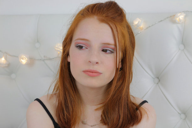 这张照片是一个14 / 15岁的红发少女，皮肤苍白，脸上有雀斑。她坐在卧室里测试眼睑上眼影的颜色，用裸唇画了夸张的眼妆，社交媒体上的化妆视频展示了全脸化妆产品的结果图片下载