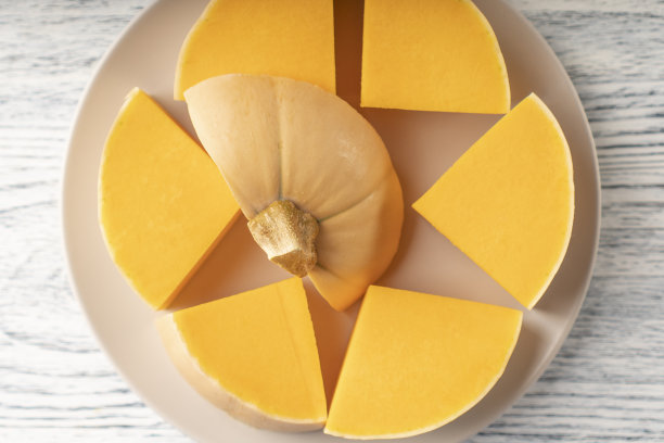 在白色和黑色的木桌上，米色的盘子上放着熟透的南瓜片图片下载