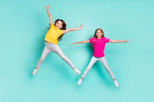 全身大小的照片，欢快的黑发金发女孩休闲跳跃与幸福漂浮在空气中，而孤立与蓝绿色的背景图片下载