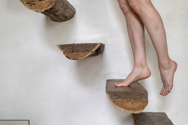 一个年轻的成年妇女站在木质台阶上，靠在白色的墙壁上。裸腿在房子与现代室内设计背景与复制空间图片下载