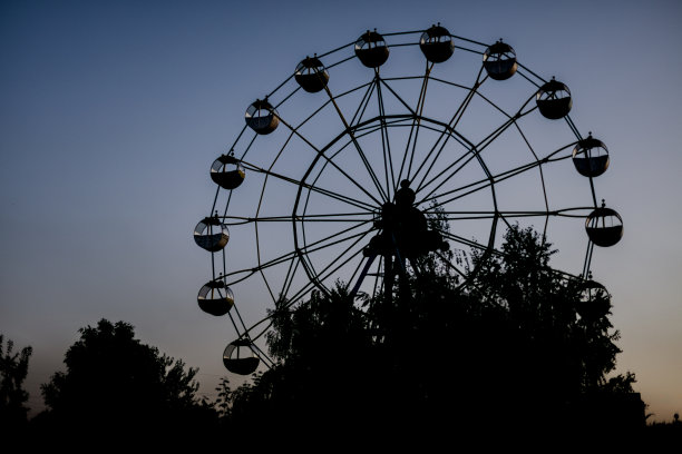 一个摩天轮的剪影在日出(日落)的太阳在树和草的背景。图片下载
