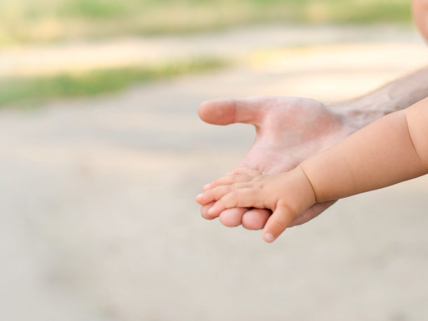 小婴儿的手与父亲的手在灯光背景与复制空间图片下载