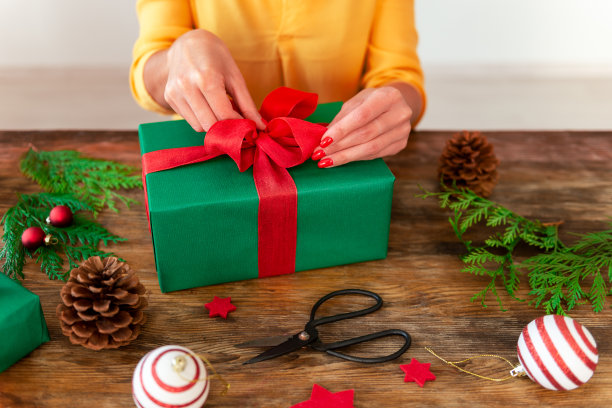 DIY礼品包装。女人在质朴的木桌上包装美丽的圣诞礼物。圣诞包装站的裁剪镜头。图片下载