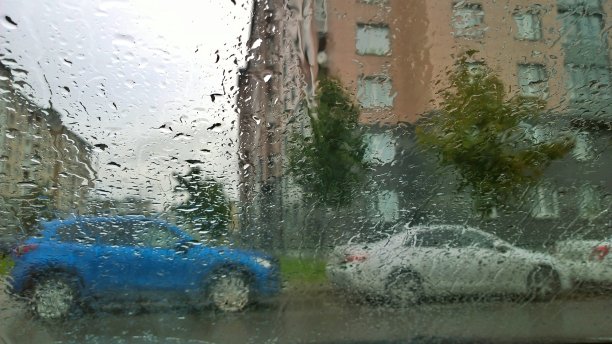 模糊抽象的形象一个城市的街道，公寓大楼和汽车透过玻璃与雨滴。阴雨绵绵，天气凄惨。透过窗户的城市景观。图片下载