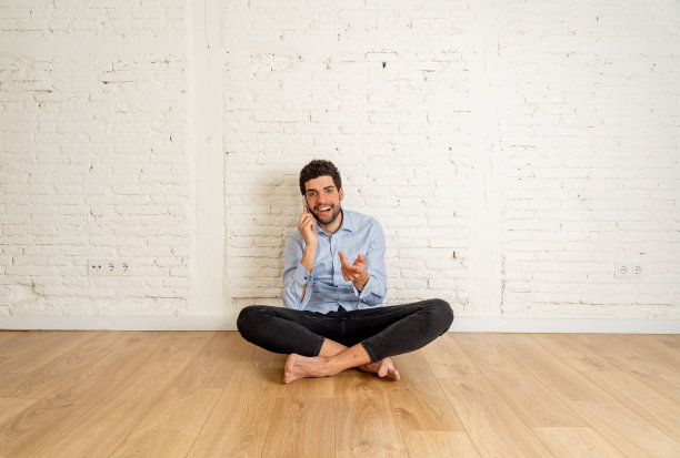 开朗的年轻潮人新主人在他的新空公寓里用智能手机说话，对他的房子投资感到高兴，准备搬家，与家人分享消息。在成功的房产购房者。图片下载