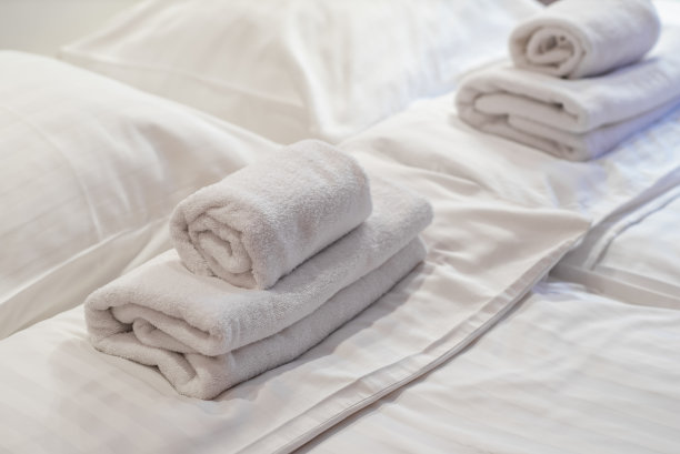 特写的毛巾卷躺在床上。白色的床单。图片下载