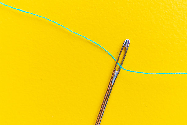 微距拍摄的针眼与一根线通过它的彩色背景图片下载