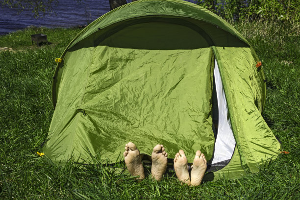 两对腿和脚后跟从绿色的帐篷中伸出在草地上图片下载