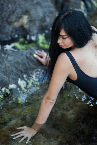 迷人的长发黑发的人休息在僻静的地方的野生岩石海岸图片下载