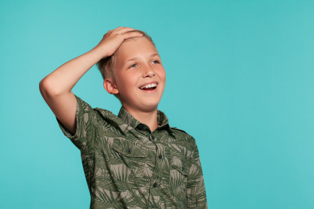 一个金发少年的特写肖像在一个蓝色的工作室背景下摆姿势的绿色衬衫与手掌印。真诚情感的概念图片下载