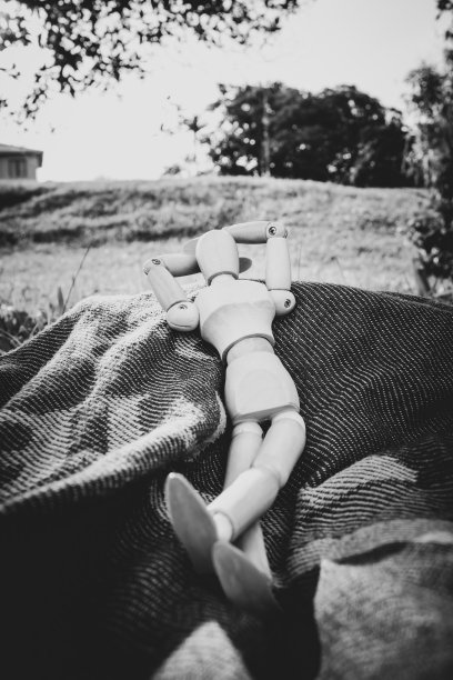 一个木制人体模型躺在户外的蓝色和绿色的毯子上放松图片下载