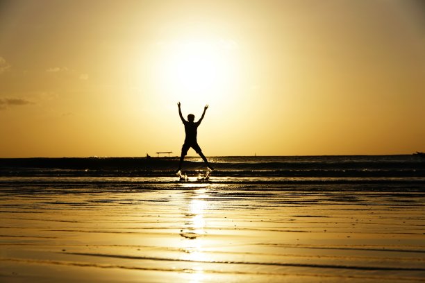 日落时分，一个人在金巴兰海滩上跳跃的剪影图片下载