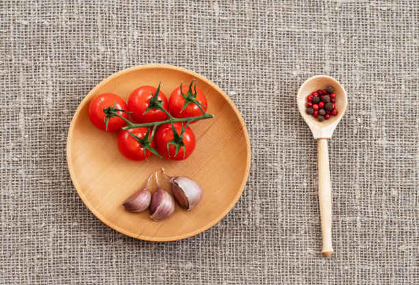 木盘里装圣女果和大蒜，粗麻布上放红黑胡椒勺。食品的背景。俯视图照片的食物，木制的菜肴。平躺图片下载