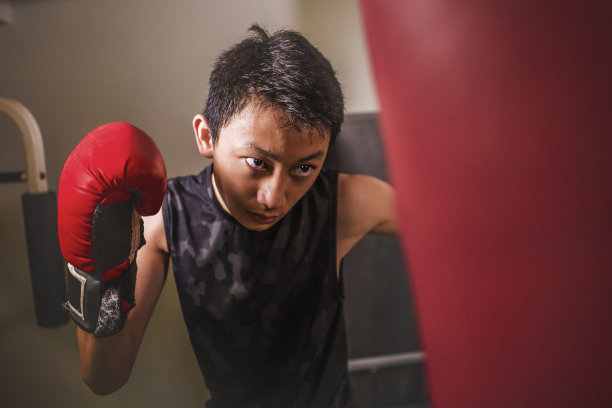 亚裔美国青少年在健身房拳击。年轻英俊和激烈的十几岁的男孩做战斗锻炼拳击沉重的包看起来很酷和坏人在健身俱乐部用手套艰苦训练图片下载