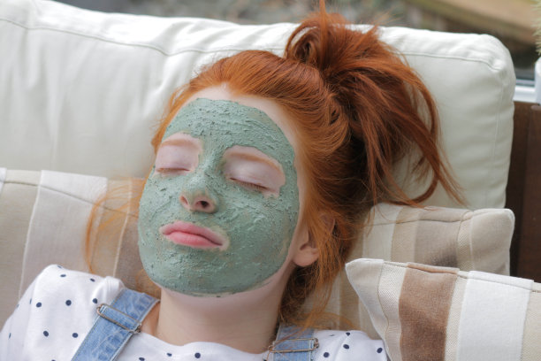 一名14 / 15岁的红发少女梳着高高的马尾辫躺在一堆沙发垫上，脸上涂着绿色的面罩图片下载