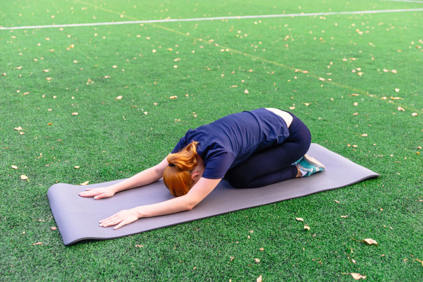 苗条美丽的女人在户外草地上的垫子上练习瑜伽。图片下载