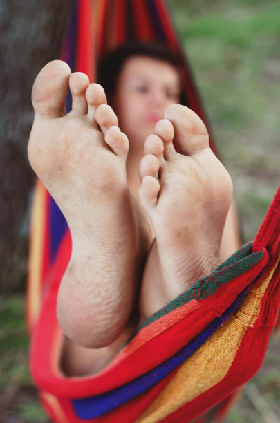 脚的特写镜头。在炎热的阳光灿烂的日子里，小伙子们在树荫下的彩色吊床上放松和日光浴。懒惰的时候图片下载