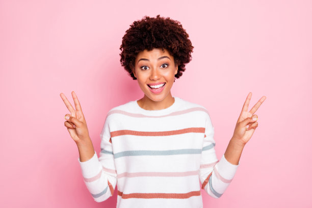 迷人的开朗可爱甜美的黑女孩的照片显示你双v标志说嗨微笑牙齿穿着白色条纹毛衣孤立在粉红色柔和的颜色背景图片下载