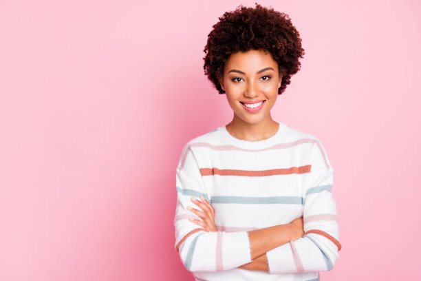 生活是美好的。照片惊人的黑皮肤商务女士工作自由职业者站着双臂交叉穿条纹套头衫孤立的粉色背景图片下载