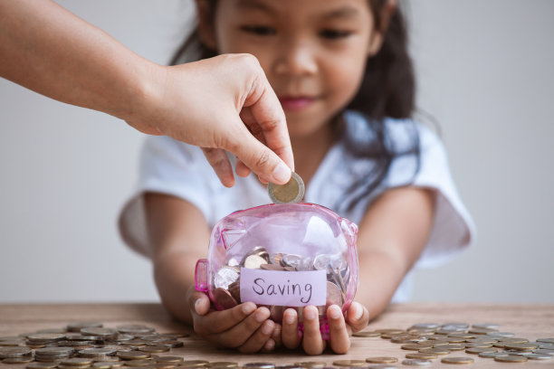 可爱的亚洲女孩抱着小猪银行和父母把钱放入小猪银行图片下载