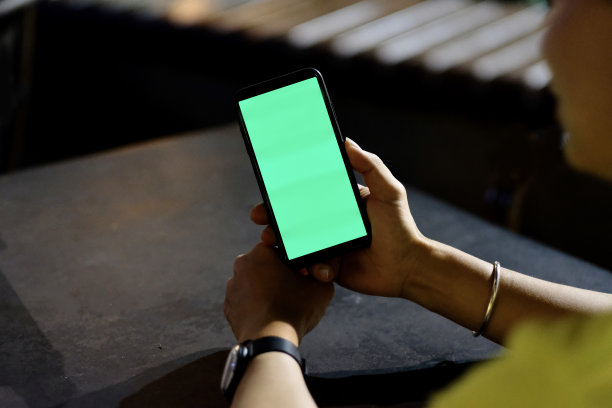 过肩视图的年轻人抱着绿色屏幕的智能手机在晚上的户外。图片下载