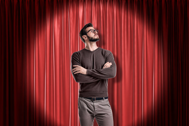 年轻男子戴着眼镜，穿着休闲服，背景是红色舞台幕布图片下载