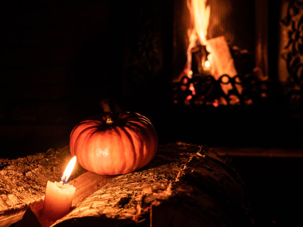 三个万圣节南瓜在黑暗中的桦木和燃烧的蜡烛上。背景是壁炉里的火焰。图片下载