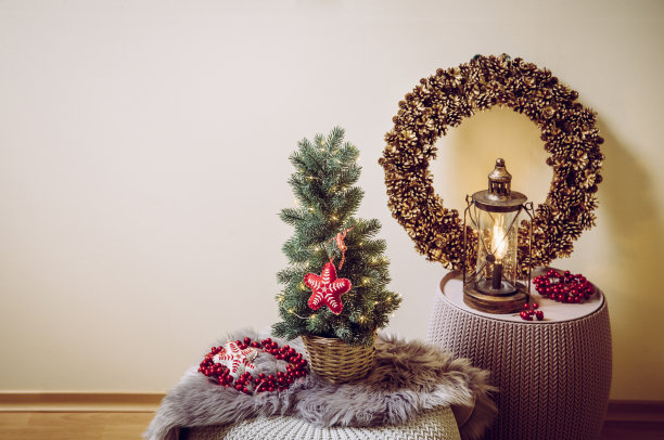 小巧便携的桌面上装饰着圣诞树，晚会彩灯亮着，红色的毛毡织物点缀着。背景上有松果花环的灯泡灯笼。复制空间的圣诞贺卡。图片下载