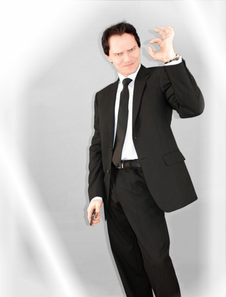 穿着西装、拿着智能手机、看着摄像头、微笑、在灰色背景上显示OK。在成功的路上。商业生活。图片下载