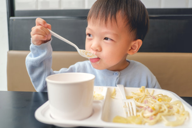 亚洲3 - 4岁的孩子在家里用勺子和叉子吃意大利面，在餐厅，美味的幼儿食物图片下载
