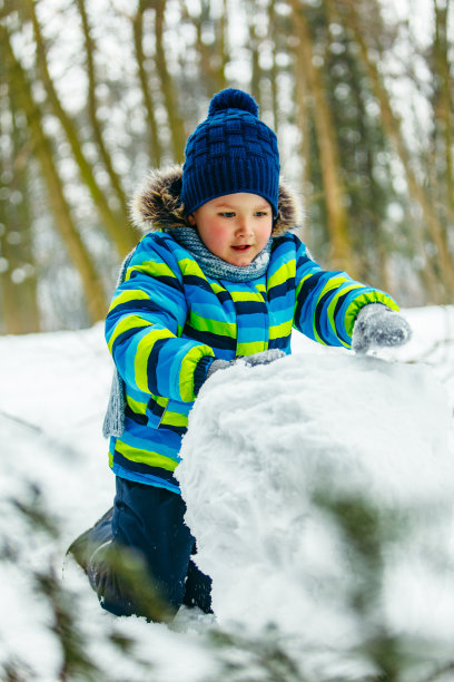 可爱的小男孩在堆雪人。滚动的大雪球。冬季休闲图片下载