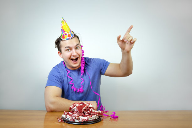 情感美丽的白种人头上戴着生日派对锥帽和皱巴巴的蛋糕抬起你的食指，快乐地微笑着。人的生活方式。图片下载