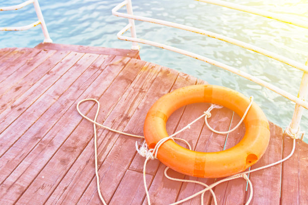 一个橙色的带绳子的救生圈，在海边的一个木制码头上。图片下载