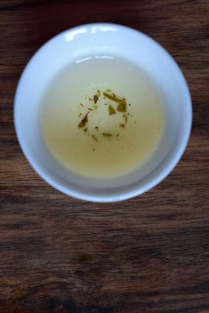 这张照片拍摄于中国茶道上，一个白色的中国小茶杯放在有空间的木桌上，剩下的绿茶和茶杯里的茶叶图片下载